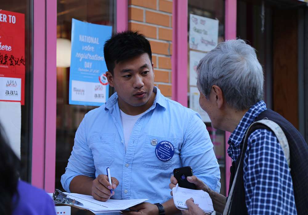 Young Asian man with vote sticker talks with older Asian woman